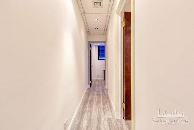 hallway featuring light wood-type flooring, visible vents, baseboards, and a drop ceiling