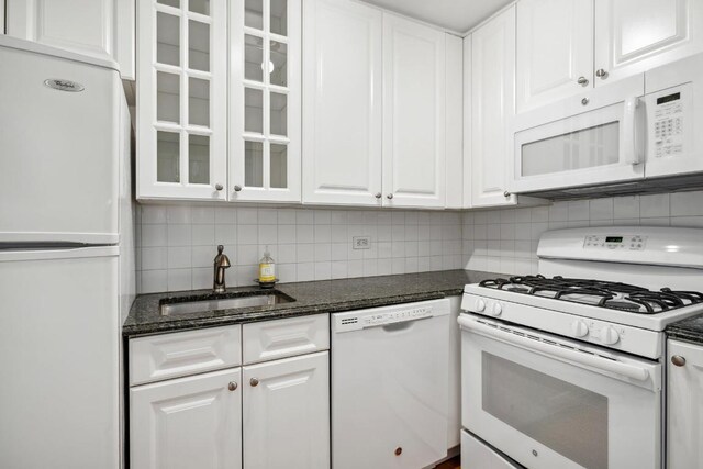 kitchen featuring sink, white appliances, white cabinetry, dark stone countertops, and tasteful backsplash