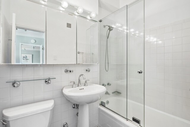 bathroom with tile walls, ornamental molding, shower / bath combination with glass door, and toilet