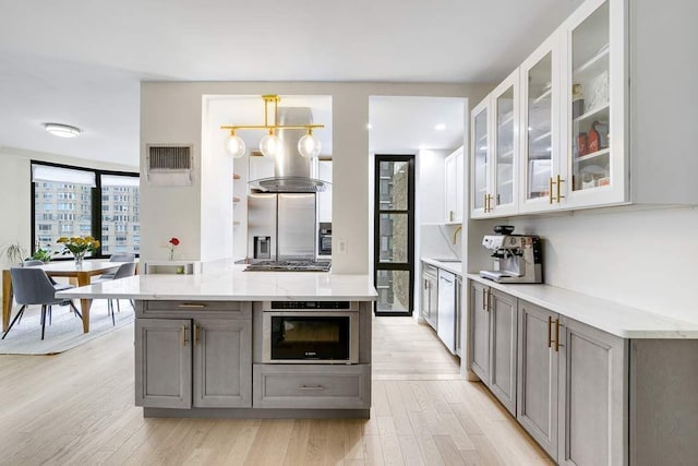 kitchen with stainless steel appliances, light stone countertops, gray cabinetry, and light hardwood / wood-style flooring