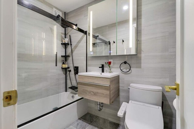 full bathroom with bath / shower combo with glass door, sink, tile walls, and toilet