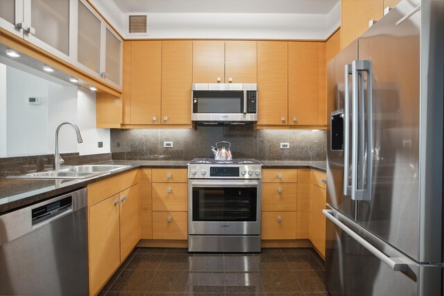 kitchen featuring stainless steel appliances, light brown cabinetry, sink, and decorative backsplash