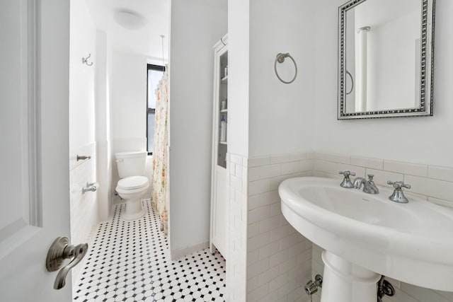 bathroom featuring a wainscoted wall, toilet, a sink, tile walls, and tile patterned flooring