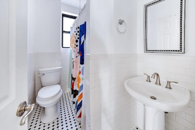 full bath with wainscoting, curtained shower, tile walls, toilet, and tile patterned floors