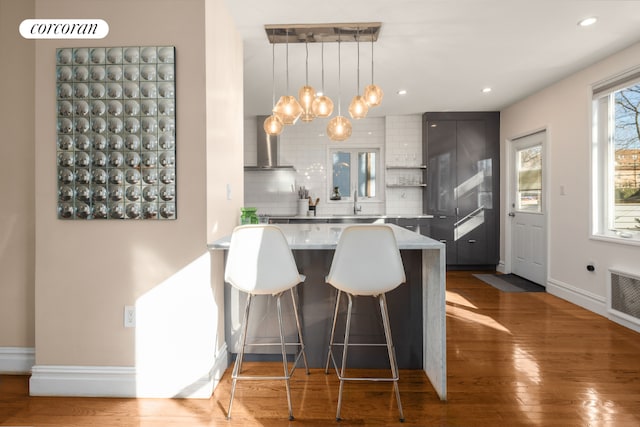 kitchen featuring kitchen peninsula, backsplash, hardwood / wood-style floors, a kitchen breakfast bar, and pendant lighting