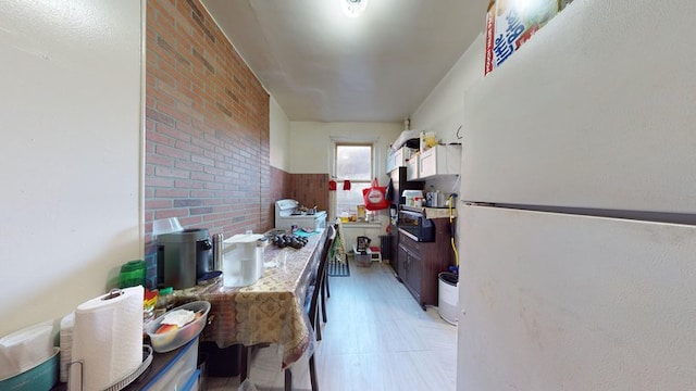 kitchen featuring light countertops, white cabinets, brick wall, and freestanding refrigerator