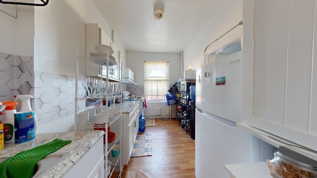 kitchen with light stone counters, light wood-type flooring, backsplash, and freestanding refrigerator