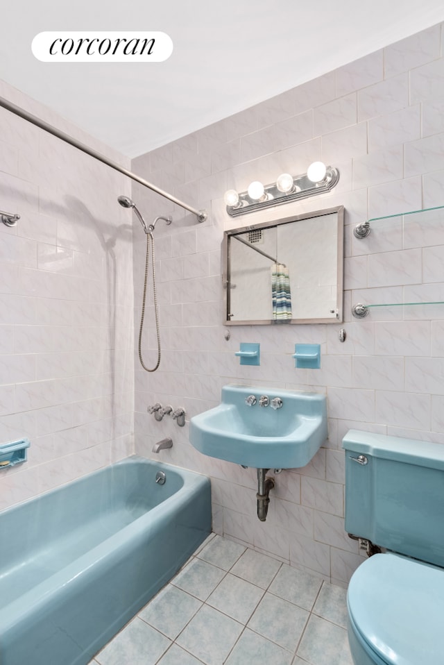 bathroom featuring tile patterned flooring, toilet, a sink, bathing tub / shower combination, and tile walls