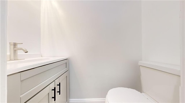 half bath featuring baseboards, toilet, and vanity