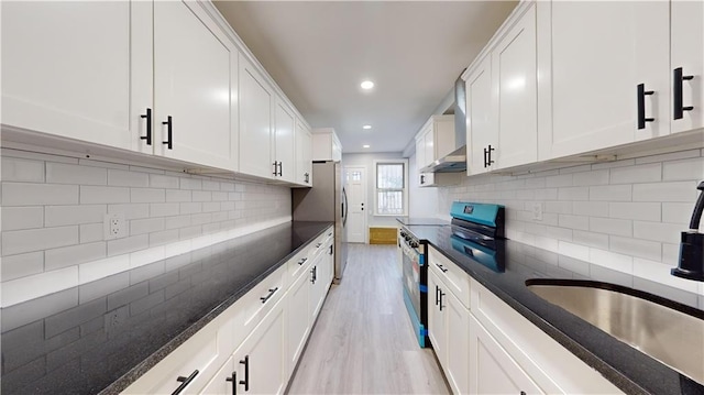 kitchen with dark stone counters, light wood-style flooring, stainless steel appliances, decorative backsplash, and white cabinetry