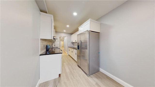 kitchen featuring light wood-style flooring, decorative backsplash, white cabinetry, dark countertops, and stainless steel fridge