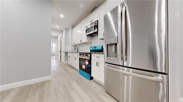 kitchen featuring baseboards, stainless steel appliances, decorative backsplash, white cabinetry, and light wood-type flooring