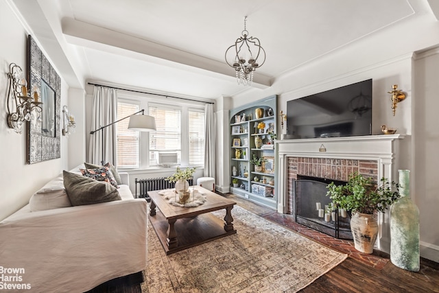 living room featuring radiator, wood finished floors, a brick fireplace, built in shelves, and beam ceiling