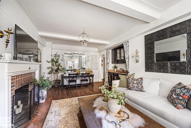 living room with an inviting chandelier, dark wood-type flooring, a brick fireplace, and beamed ceiling