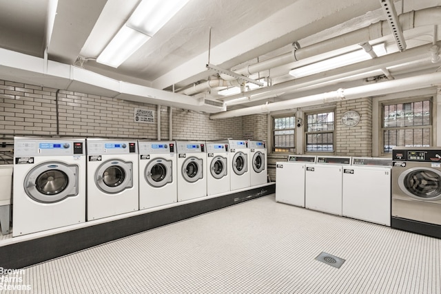 community laundry room with tile patterned floors, brick wall, and separate washer and dryer