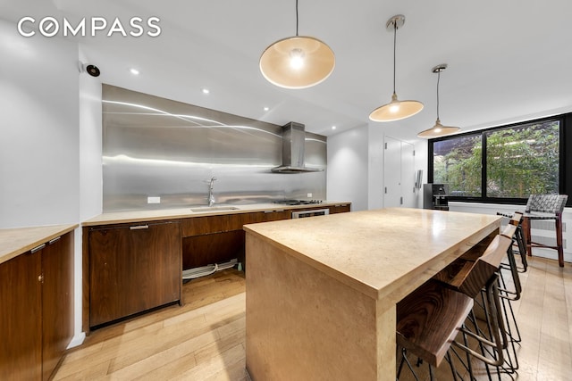 kitchen featuring light wood-type flooring, a sink, a kitchen island, wall chimney exhaust hood, and light countertops