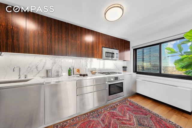 kitchen with a sink, light wood-type flooring, appliances with stainless steel finishes, and light countertops