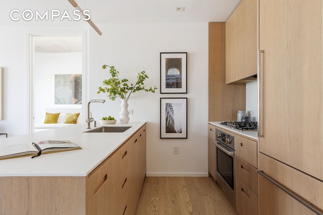 kitchen featuring stainless steel appliances, a peninsula, a sink, light countertops, and light brown cabinetry