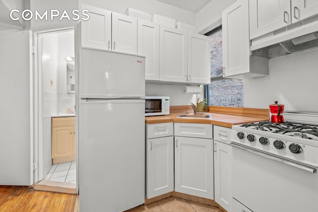 kitchen featuring white appliances, light tile patterned floors, a sink, under cabinet range hood, and white cabinetry