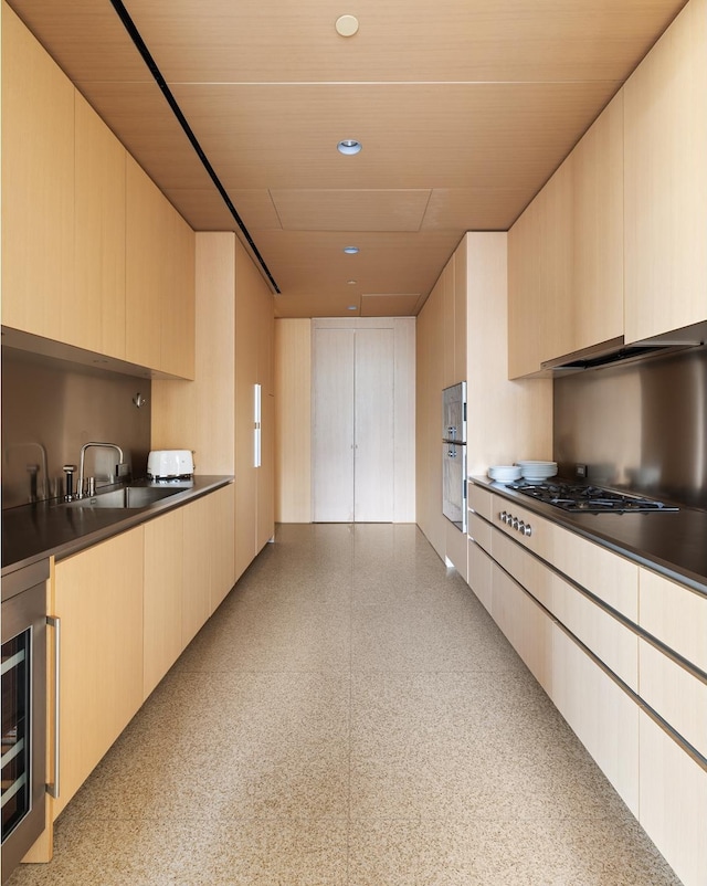 kitchen with under cabinet range hood, dark countertops, gas stovetop, a sink, and wine cooler