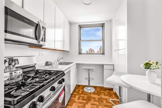 kitchen featuring light parquet flooring, appliances with stainless steel finishes, sink, and white cabinets