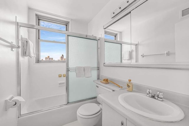 full bathroom with bath / shower combo with glass door, a healthy amount of sunlight, vanity, and toilet