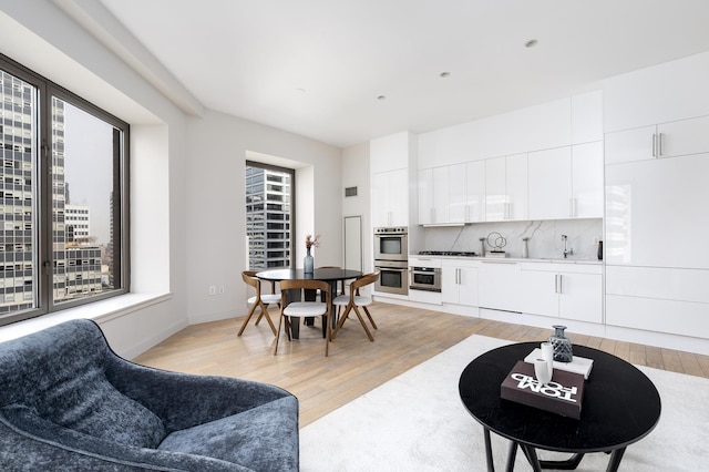 kitchen with light wood-style floors, backsplash, white cabinets, double oven, and modern cabinets