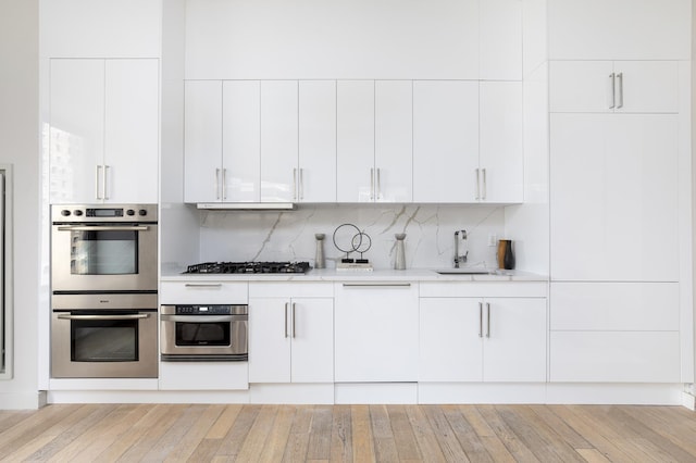 kitchen featuring appliances with stainless steel finishes, a sink, white cabinets, tasteful backsplash, and light wood-type flooring
