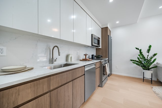 kitchen with white cabinetry, appliances with stainless steel finishes, sink, and light stone counters