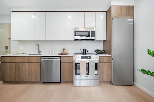 kitchen with sink, backsplash, white cabinets, and appliances with stainless steel finishes