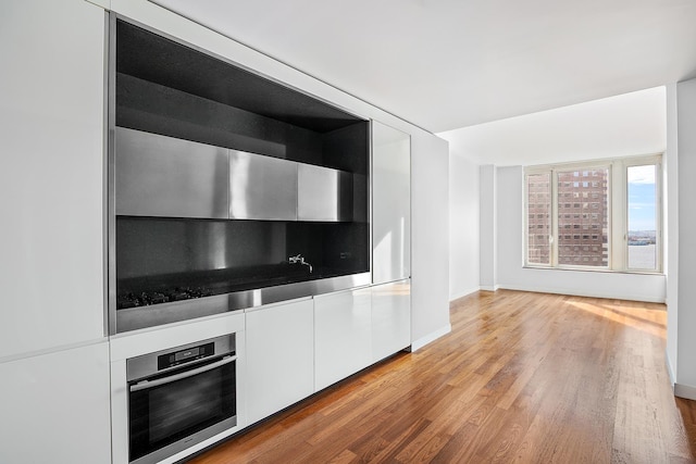 kitchen featuring stainless steel oven, baseboards, light wood-style floors, white cabinetry, and decorative backsplash