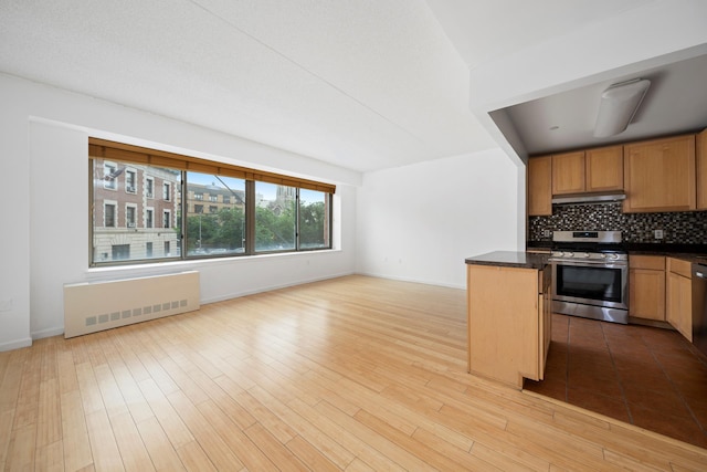 kitchen with under cabinet range hood, dark countertops, radiator, stainless steel range with gas cooktop, and decorative backsplash