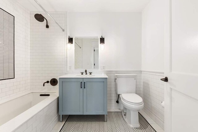 full bathroom featuring toilet, tiled shower / bath, tile walls, vanity, and tile patterned flooring