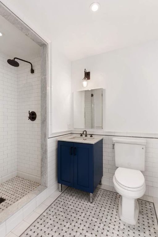 bathroom with tile walls, a tile shower, vanity, tile patterned floors, and toilet