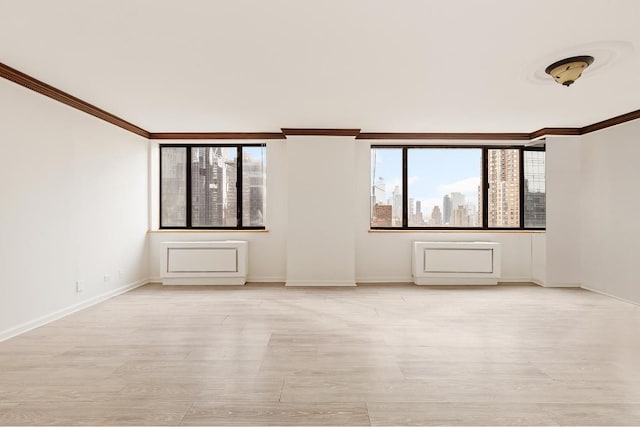 empty room with ornamental molding, a city view, light wood-style flooring, and baseboards