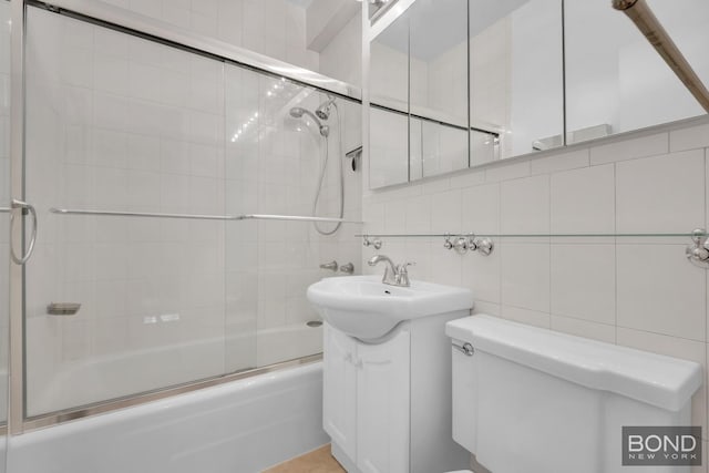 bathroom featuring toilet, shower / bath combination with glass door, tile walls, decorative backsplash, and vanity