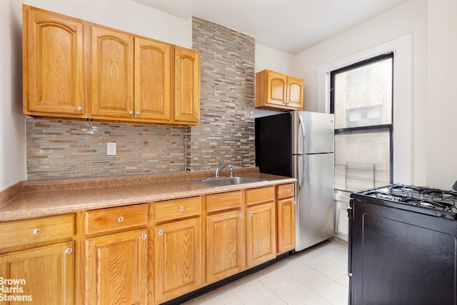 kitchen featuring black gas range oven, decorative backsplash, freestanding refrigerator, light tile patterned flooring, and a sink