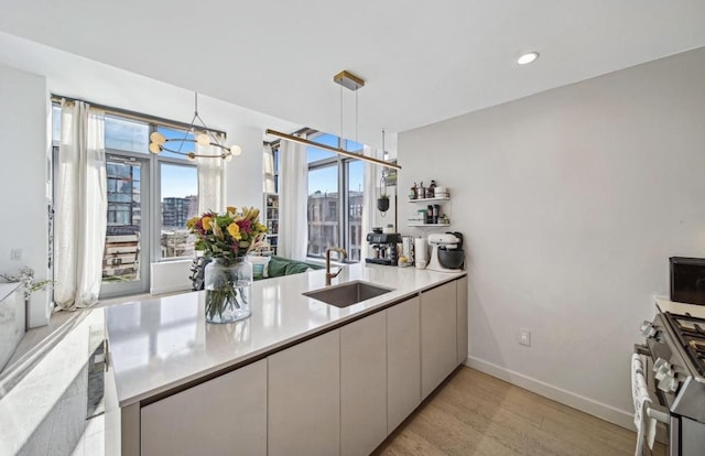 kitchen featuring sink, stainless steel gas stove, light hardwood / wood-style flooring, hanging light fixtures, and a notable chandelier