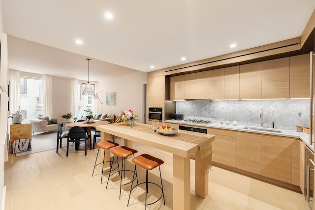 kitchen featuring a sink, stainless steel oven, a kitchen bar, modern cabinets, and light brown cabinets