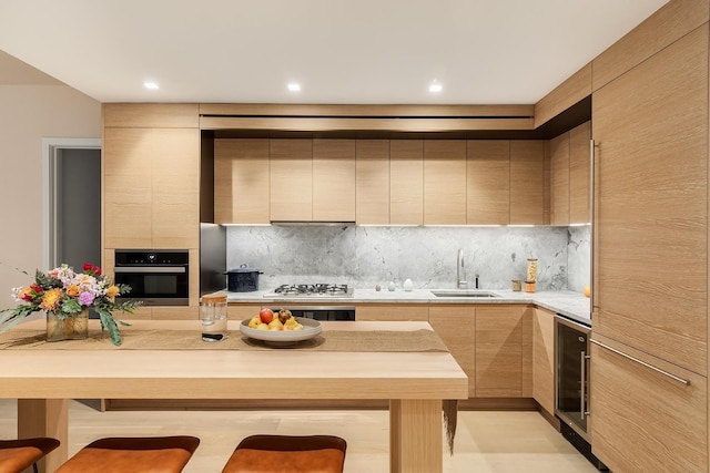 kitchen with a sink, light brown cabinetry, modern cabinets, light countertops, and wall oven