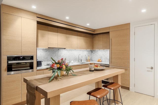 kitchen with light countertops, backsplash, a breakfast bar, a sink, and stainless steel oven