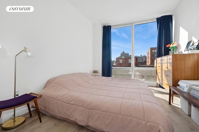 bedroom with visible vents, floor to ceiling windows, a view of city, and wood finished floors