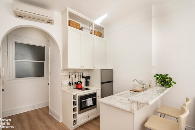 kitchen featuring light wood-type flooring, a wall mounted air conditioner, appliances with stainless steel finishes, and a peninsula