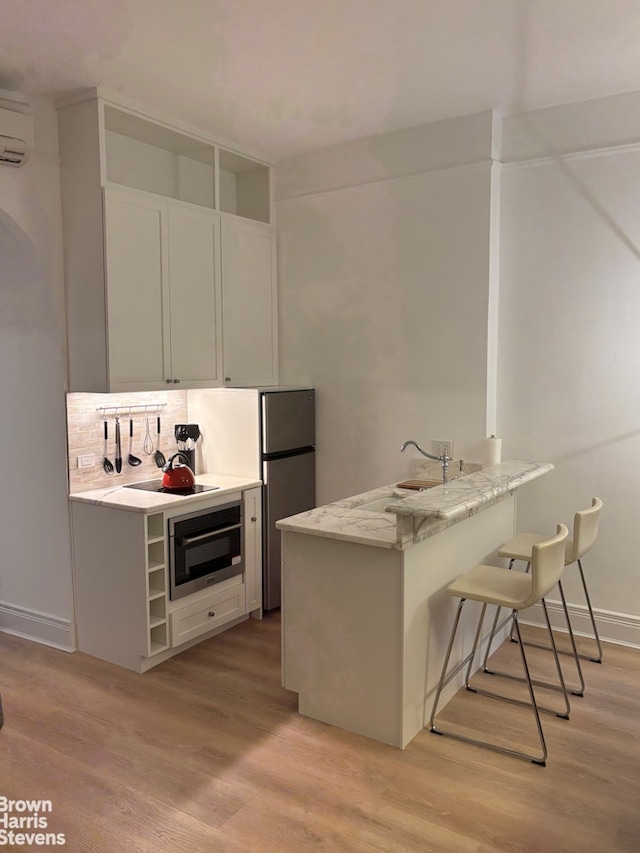 kitchen with a peninsula, a sink, oven, light wood-style floors, and a kitchen breakfast bar