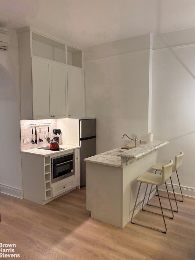 kitchen with a kitchen bar, oven, a sink, light wood-style floors, and a peninsula
