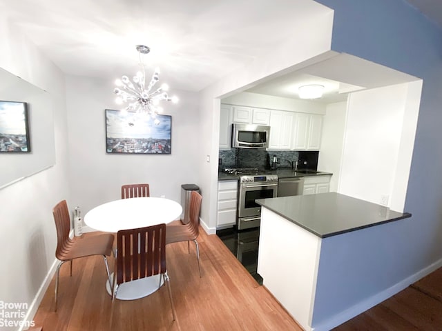 kitchen featuring dark countertops, hanging light fixtures, backsplash, appliances with stainless steel finishes, and white cabinets