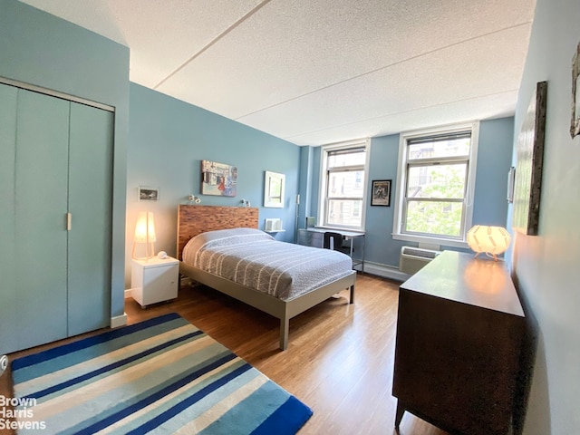 bedroom featuring a closet, a wall unit AC, light wood-style flooring, and a textured ceiling