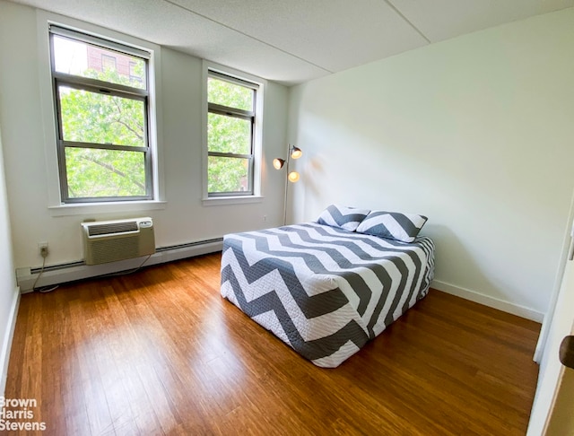 bedroom featuring a baseboard heating unit, a wall mounted AC, baseboards, and wood finished floors