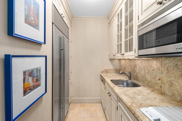 kitchen featuring a sink, glass insert cabinets, appliances with stainless steel finishes, decorative backsplash, and light stone countertops