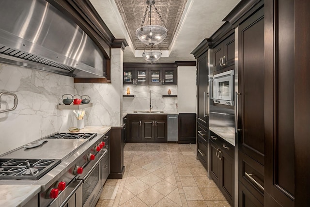 kitchen featuring double oven range, a tray ceiling, a sink, decorative backsplash, and wall chimney range hood